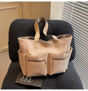 Detail view of khaki canvas tote bag featuring dual front zipper pockets and side slots