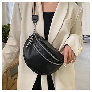 Detail of black quilted crossbody bag with silver zippers and striped strap