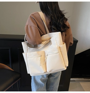 Detail of a beige canvas tote bag showing multiple pockets and wide shoulder straps