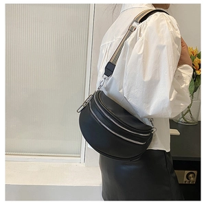 Detail view of black crescent crossbody bag with double silver zippers and striped strap