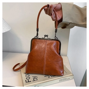 Close-up of vintage brown leather frame bag with metal clasp and top handle on books