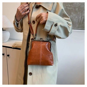 Close-up of brown leather kiss-lock bag with white stitching detail worn with beige coat