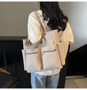 Detail of beige canvas tote bag showing zippered front pockets and woven shoulder strap
