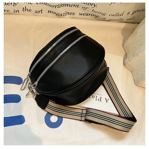 Detail of black pebbled leather crossbody bag featuring dual silver zippers and striped strap