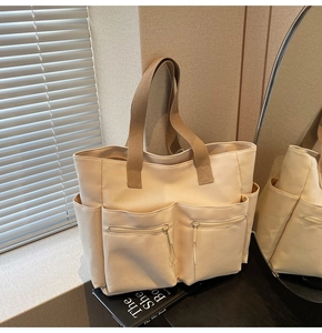 Detailed close-up of a large beige canvas tote bag with front zippers and brown straps