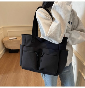 Detail of a large black canvas tote bag with functional double front zipper pockets