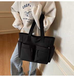 Close-up of black canvas tote bag showing multiple zipper pockets and wide shoulder straps