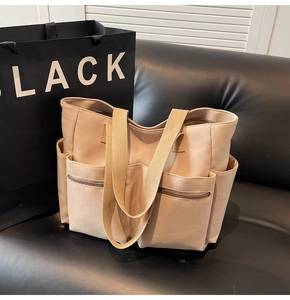 Detail of khaki canvas tote bag showing dual front zip pockets and wide shoulder strap