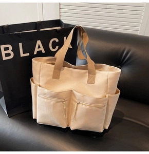 Detail of canvas tote bag with brown straps and functional multiple front zip pockets