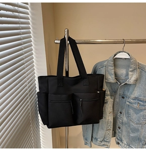 Detail of black canvas tote bag showing functional front zipper pockets and side pockets