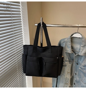 Detail of black canvas tote bag showing multiple functional pockets and durable handles