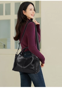 Detail of black glossy leather handbag showing handle and adjustable shoulder strap