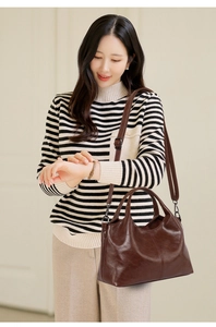 Detail of dark brown leather tote bag with adjustable strap worn by model in soft light