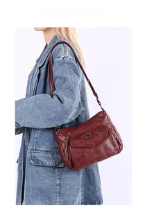 Detail of burgundy soft leather crossbody bag featuring stitched texture and silver zippers