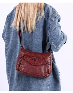 Detail of burgundy soft leather crossbody bag with multiple zippers and woven flap texture