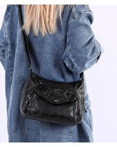 Detailed side view of black soft leather crossbody bag with multiple zippers on blue denim