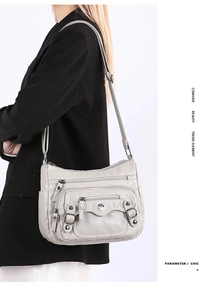 Close-up of light gray cowhide crossbody bag with multiple functional zippers and buckle details