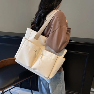 Large beige canvas tote bag with wide khaki shoulder strap and front zipper pockets