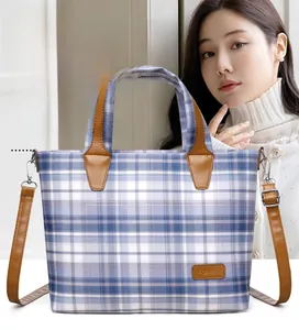 Detail view of blue plaid tote bag featuring brown leather handles and side buckle
