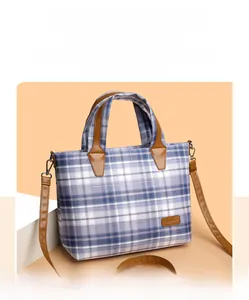 Detail of blue plaid tote bag featuring brown leather handles and a classic brand patch