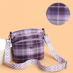 Close-up of purple plaid crossbody bag with multiple zippers and woven shoulder strap