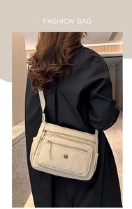 Detail of beige nylon crossbody bag with multiple zippers and adjustable strap on a model
