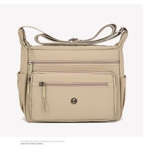 Close-up of the beige nylon shoulder bag showing multiple zipper pockets and front metal logo
