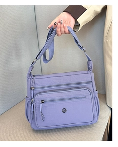 Detail view of lavender nylon crossbody bag with multi-zipper pockets and wide strap