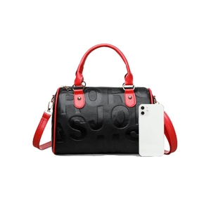 Black pebbled leather Boston bag with red handles and gold hardware, shown with phone