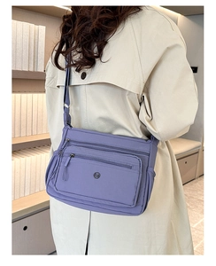 Detail of a purple nylon crossbody bag with multiple zippers worn with a beige coat