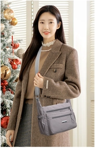 Detail of grey nylon crossbody bag with multiple zip pockets shown in a cozy indoor setting