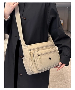 Detail of multi-pocket nylon crossbody bag showing zip compartments and side pocket