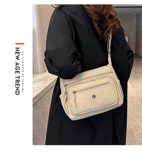 Detailed view of beige multi-zipper nylon crossbody bag worn by model over a black coat
