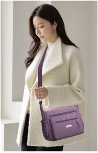 Detail view of purple nylon crossbody bag with three zipper layers and adjustable strap