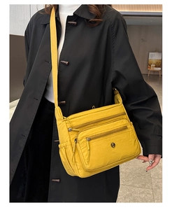 Detail of bright yellow nylon crossbody bag featuring multiple zipper pockets and logo