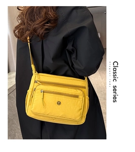 Detail of a bright yellow nylon crossbody bag with multiple zippers and round metal logo