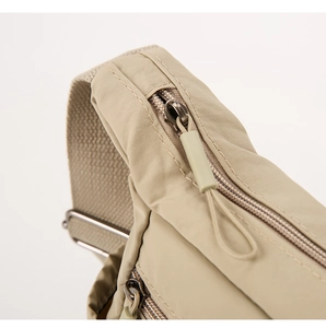 Close-up of smooth metal zippers and durable nylon fabric on a beige crossbody bag