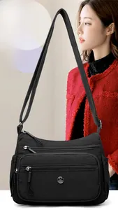 Détail du sac bandoulière en nylon noir avec poches zippées porté sur une veste en tweed rouge