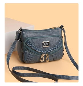 Detail view of smog blue leather crossbody bag showing multi-layered zippers and S sport logo