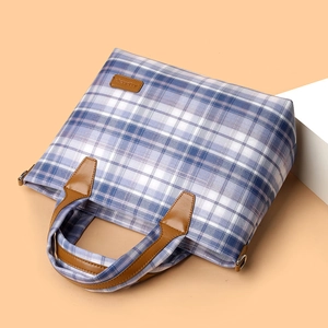 Blue and purple plaid tote bag with brown leather handles on a pink background