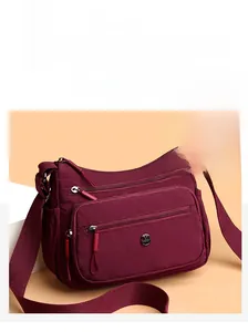 Détail du sac bandoulière en nylon bordeaux avec plusieurs compartiments zippés et sangle