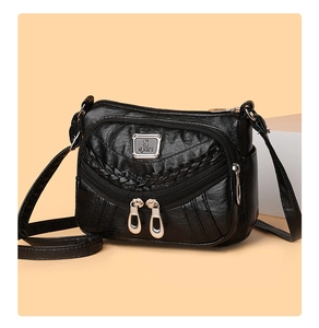 Detail of black faux leather crossbody bag with woven elements and multiple zipper pockets