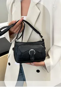 Close-up of black litchi grain leather crossbody bag with silver buckle on beige suit