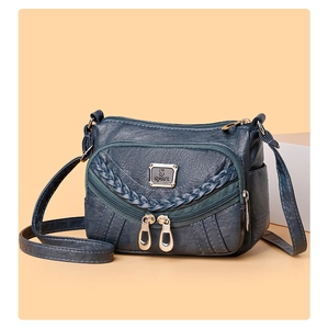 Detail of dark teal faux leather crossbody bag with dual zipper layers and braided trim