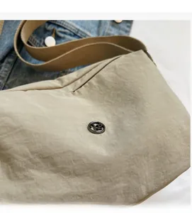 Detail of light khaki dumpling bag with metallic logo and wide fabric strap on denim