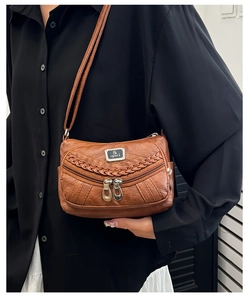 Close-up of brown soft leather crossbody bag with woven trim and metal zipper pockets