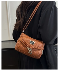Detail of brown faux leather crossbody bag with woven trim and double zippers worn by model