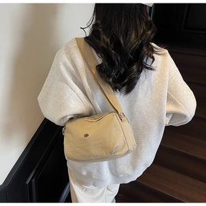 Detail view of beige nylon dumpling bag with wide strap on model climbing wooden stairs