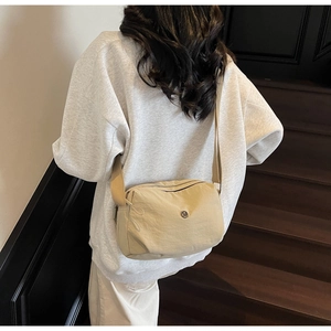 Close-up of a beige nylon crescent crossbody bag with metal logo and wide strap