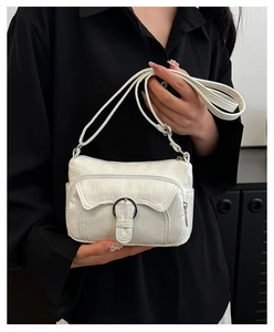Close-up of white pleated leather crossbody bag with silver metal ring buckle and strap